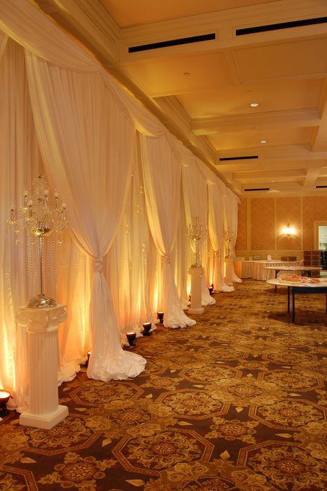 White Backdrop with Amber LED Up Lighting #whitechiffon #fabricbackdrop #amberuplighting #uplighting #AmberLED #weddingbackdrop #weddingdecor #michiganweddings #colonialevents Wedding Wall Drapes, Backdrop Lighting Ideas, Met Gala Design, Quince List, Gold Shimmer Background, Yellow Quince, Event Space Decor, Outdoor Christmas Party, Wall Drapes