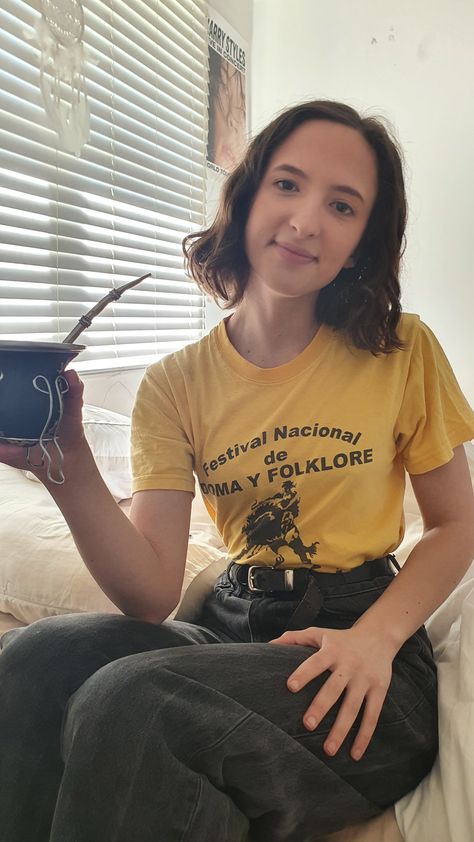 Woman in yellow graphic tee, tucked into black jeans. Sitting drinking maté. Graphic Tee Tucked Into Jeans, Yellow Graphic Tee Outfit, Black Shirt Outfits, Yellow Graphic Tee, Brocade Blouse Designs, Brocade Blouse, Graphic Tee Outfits, Brocade Blouses, Yellow Pants