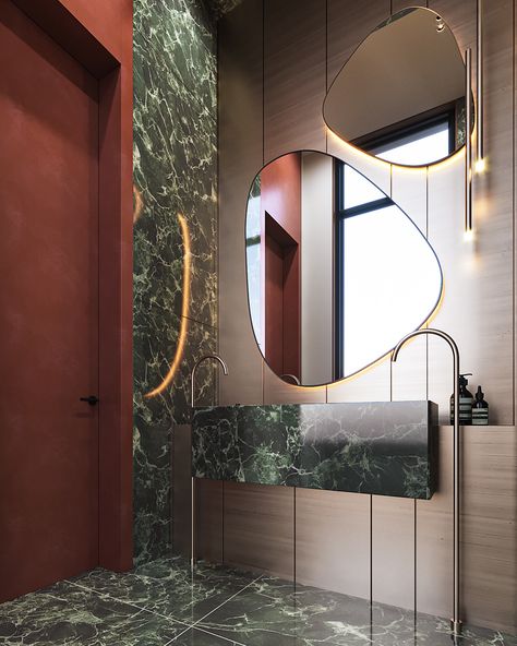 This elegant bathroom design in Riyadh blends luxurious materials and contemporary aesthetics. The dark green marble, used extensively on the walls and floors, adds a touch of sophistication and opulence 💎, while the organic-shaped mirrors paired with ambient lighting create a modern, artistic vibe 🎨. The copper accents on the faucets and fixtures add warmth and a refined contrast to the cool-toned marble, making the space feel inviting and chic 🌟. The statement wall behind the toilet, ad... Dark Green Marble, Elegant Bathroom Design, Artistic Vibe, Copper Accents, Statement Wall, Elegant Bathroom, Green Marble, Riyadh, Organic Shapes