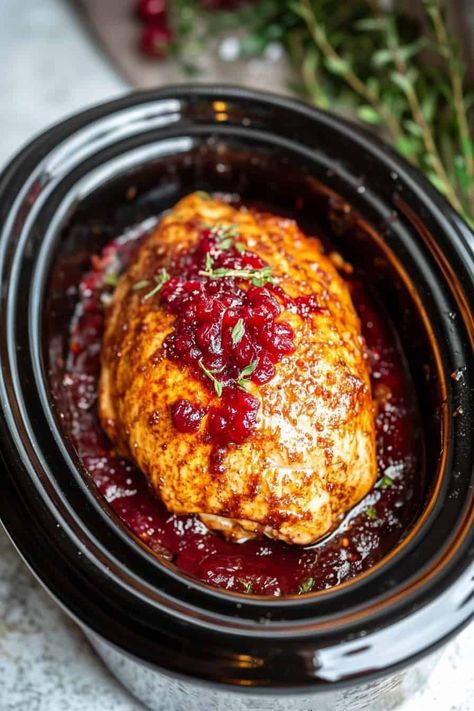 The turkey breast cooking inside a CrockPot, bathed in cranberry sauce and garnished with herbs, hinting at the flavorful result to come. Turkey Breast Crockpot Cranberry Sauce, Turkey Cranberry Crockpot, Cranberry Orange Turkey Breast Crockpot, Crock Pot Turkey Breast With Cranberry, Crock Pot Turkey Breast With Cranberry Sauce, Turkey Breast With Cranberries In Crockpot, Ground Turkey Cranberry Recipes, Turkey Dinner Crockpot Recipes, Easy Crock Pot Christmas Dinner