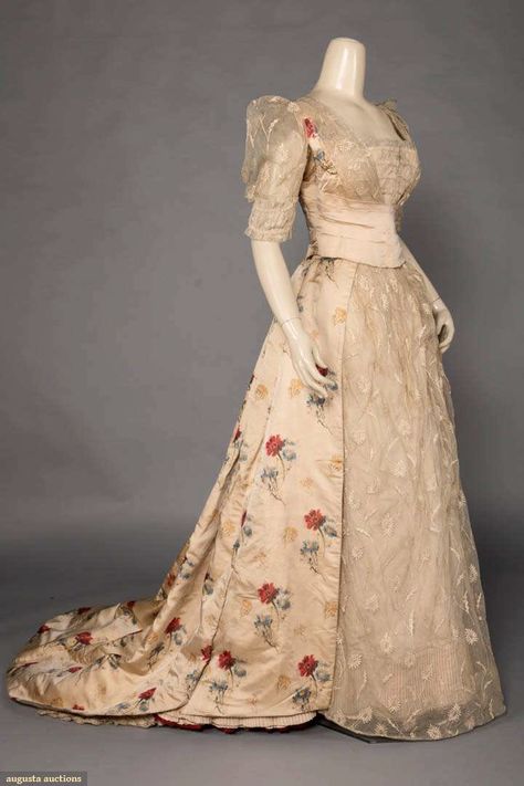 Up for auction March 28, 2020 - Historic Fashion Online Bellows Falls Trained evening gown of blond silk satin w/ warp-printed red, yellow & blue flowers over embroidered net, w/ satin cummerbund sash closure, originally 1880s, altered c. 1900, B 33", W 23", L 58-77", (underarms worn, few tiny holes/ wear to back of skirt , train dirty, wear to net at CF closure) good. MCNY Victorian Evening Gown, 1880s Dress, 1900s Costume, Yellow Blue Flowers, Historical Gowns, Silk Evening Gown, Historic Fashion, Era Fashion, Old Dresses