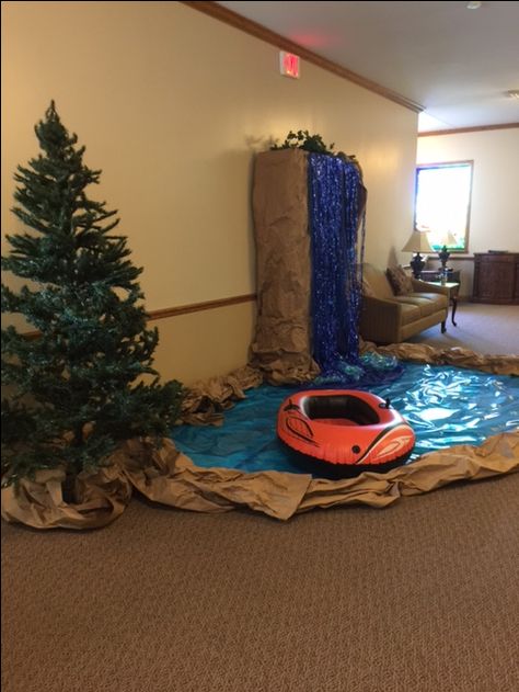 This river/camping scene can work for any spot in your church. This one was used in the foyer area of the church! Display evergreen trees. Create a pond/river using brown craft paper and blue  and cellophane paper. The waterfall was created using a large piece of furniture that is part of the foyer. Great idea to cover what is there! Cover the display case with brown paper. Add blue paper along with foil curtains to give the look and feel of a waterfall! And add a raft!! Camp Out Vbs, Vbs Decorating Ideas, Zelt Camping Hacks, Camp Vbs, Zelt Camping, Camping Classroom, Camping Theme Classroom, Indoor Camping, Camping Theme Party