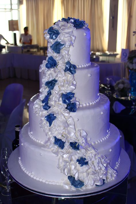 4 layer white wedding cake with cascading white and navy blue ruffles White And Royal Blue Wedding Dress, Royal Blue White And Silver Wedding Cake, Blue Black And White Wedding Theme, Quince Cakes Royal Blue And Silver, Dark Blue And White Quinceanera Dresses, Navy Blue And White Quinceanera Dresses, Royal Blue Black And White Wedding, Dark Blue And White Cake, Royal Blue And White Wedding Cake