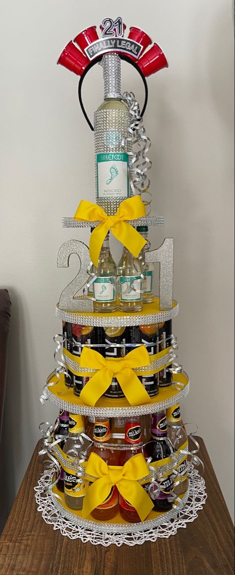 21st birthday alcohol tower four tiers decorated with silver gems and yellow bows. Truly Cake Tower, 21st Alcohol Tower, 21 Alcohol Cake Tower, Booze Cake Tower, Yellow 21st Birthday Ideas, Shot Cake Ideas, 2 Tier 21st Birthday Cake, Alcohol Tower 21st Birthday, Alcohol Cake Tower