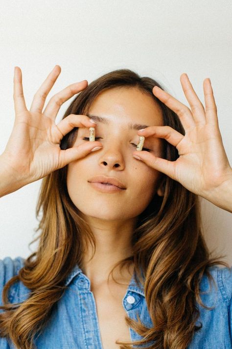 Portrait shot of a brunette model holding up two vitamins over each of her eyes. They are placed in her thumb and pointer finger with her other fingers pointing up in the air. She is wearing a denim shirt. Lifestyle Vitamin Photography, Vitamins Photoshoot, Vitamin Product Photography, Vitamin Photography, Commercial Photography Model, Take Your Vitamins, Model Photoshop, Colorful Photography, Product Photoshoot