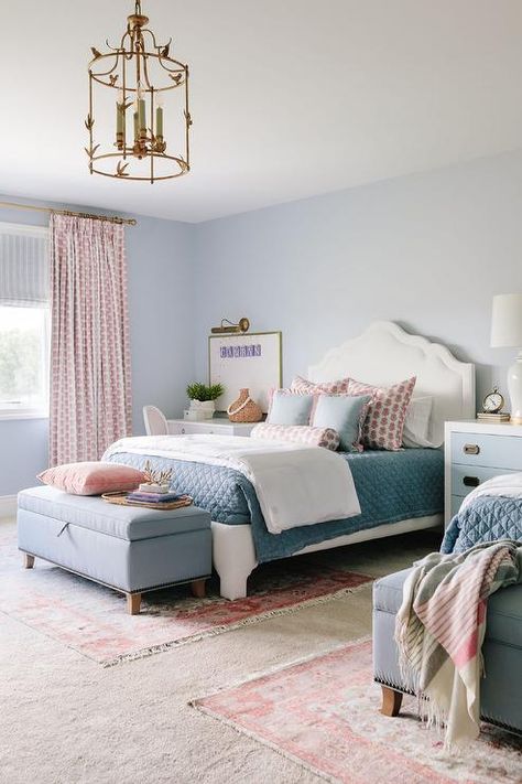 Shared pink and blue girls' bedroom features white fabric twin beds placed on layered rugs in front of a light blue wall on either side of a white and blue dresser nightstand lit by a white lamp. Light Blue Pink Bedroom, Pink And Blue Girls Bedroom, Light Blue Girls Bedroom, 2 Color Wall, Light Blue And Pink Bedroom, Girls Bedroom Blue, Blue And Pink Room, Pink And Blue Room, Blue Girls Bedroom