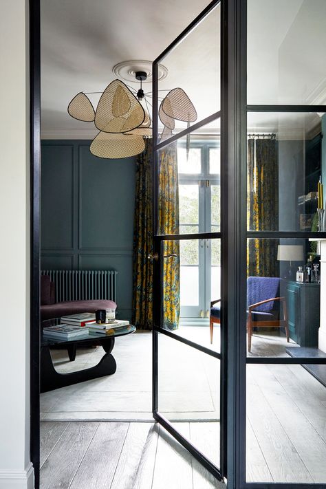 Internal Crittall Doors and a fixed panel frame the view into this panelled living room. A deep moody green-blue on the walls is paired with a stone coloured ceiling and feature cane pendant light. House of Hackney curtains frame the french doors overlooking the garden. Designed by A New Day Interior Design Studio Crittal Doors Extension, Lodge Entrance, Crittall Doors, Crittal Doors, Industrial Living Room, Snug Room, House Staircase, Imperial Beach, Online Interior Design Services