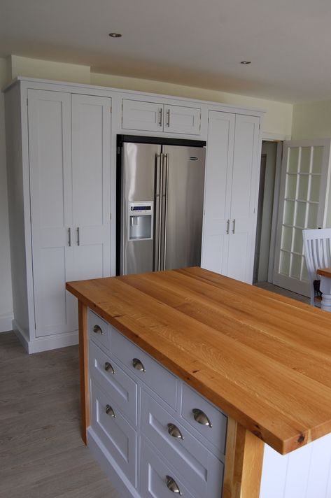 A contemporary American style fridge freezer is built in to this Hand Painted Kitchen by a surround of larder cupboards.  The island has an interesting combination of oak top and frame with painted base. Oak Pantry, Cosy Home Decor, Utility Room Designs, American Fridge Freezer, Modern Country Kitchens, Kitchen Printables, Pantry Fridge, American Fridge, Pantry Cabinets