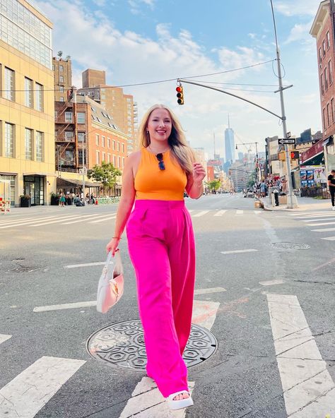 Sarah is wearing bright pink wide leg pants and an an orange top. She has a white handbag and white platform sandals. In the background you can see the One World Trade Center in the background. Downtown Brunch Outfit, Colorful Bar Outfit, Summer Outfit Inspiration Midsize, Colorful Summer Outfits Midsize, Colourful Outfits Midsize, Mid Size Fashion Colorful, Quirky Midsize Fashion, Bright Colored Outfits Plus Size, Curvy Midsize Outfits Summer