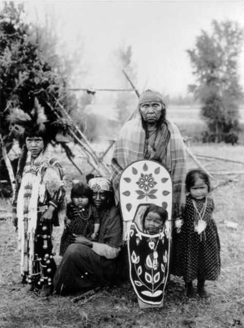 Group portrait of Flathead (Salish) Native Americans, identified as the wife, mother, and children of Lalasee. The eldest woman wears a print dress, a shawl, and a headband. The younger woman wears a print dress and a headband. The two young girls wear print dresses and necklaces. The young boy wears leggings with bells, a print shirt, an ornamental neckpiece, fur strips, and a traditional Flathead hair style. The infant is in a cradleboard decorated in a flower motif. Date 	1907: Indian Dog, Native Clothing, Native Beauty, Native Culture, Aboriginal American, Indian History Facts, American Indian History, Black Indians, Native American Photos