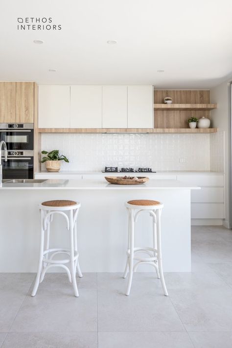 White and wood kitchen with light grey porcelain tile floors. White stone benchtops and a white square tile feature on the splashback. There are 2 white wood and rattan bar stools in front of the island bench, which holds a kitchen sink with chrome mixer. Square Textured Tile, Stone Benchtop Kitchen, Porcelain Tile Floor Kitchen, Grey Kitchen Tiles, Modern Coastal Kitchen, Modern Kitchen Tiles, White Kitchen Lighting, White Kitchen Splashback, White Wood Kitchens