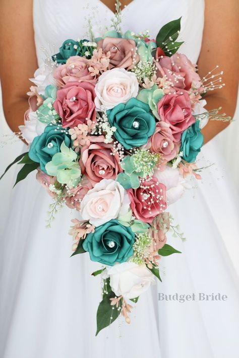 This brides’ bouquet is the perfect option if you have chosen a classic theme for your wedding. A lovely array of dusty rose and mauve are center-stage in this stunning arrangement. This bouquet is made with dusty rose-colored roses, mauve roses, barely pink roses and teal roses all accented by pearls and rhinestones. As always, this bouquet has been wired by hand and designed by our in-house florists - you can rest assured that our bouquets will maintain their quality and stand the test of time Teal And Blush Pink Wedding, Teal Pink And Gold Wedding, Teal And Coral Wedding Ideas, Pink And Turquoise Wedding Decorations, Teal And Pink Wedding Bouquet, Pink And Turquoise Wedding Theme, Coral And Teal Wedding Bouquet, Rose Gold And Teal Wedding Theme, Teal And Pink Wedding Ideas