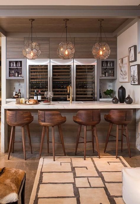 Three Arteriors Beck Pendants illuminating a marble waterfall bar fitted with a wet bar sink and gold gooseneck faucet lined with wood counter stools. Contemporary Basement, Basement Bar Design, Rustic Basement, Basement Bar Designs, Wood Backsplash, Basement Kitchen, Herringbone Backsplash, Small Basements, Home Bar Designs