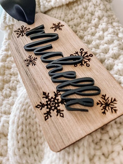 "- Personalized Wooden Stocking Name Tag -  This stocking tag is beautiful, chic and the perfect addition to your Christmas stocking.   This stocking tag is made of 1/8\" birch and measures 2.5\" wide x 5.5\" long.  A beautiful 1.5\" wide satin ribbon has been added for easy hanging and fray check has been added to prevent fraying.    The name has been laser cut and is made of 1/8\" acrylic.  The background of the tag has snowflakes that have been laser engraved into the wood." Wooden Laser Crafts, Easy Glowforge Projects, Laser Made Gifts, Holiday Laser Projects, Christmas Stocking Name Tag Ideas, Cricut Christmas Stockings, Laser Cnc Projects, Cricut Stocking Tags, Laser Business Ideas