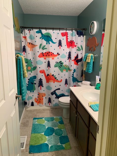 Wall dinosaurs are from Hobby Lobby. The wall clock, shower curtain, bath rug, and towels are from Amazon. The toothbrush holder is from Target. Dino Themed Bathroom, Dinosaur Theme Bathroom, Dino Bathroom Decor, Kid Boy Bathroom, Dino Themed Room, Toddler Bathroom Organization, Dino Bathroom Ideas, Dinosaur Themed Bathroom, Boy Bathroom Ideas Kid