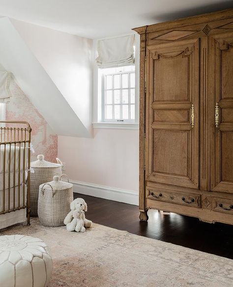 Pink French girl's nursery features a French armoire accented with antique brass hardware and placed on a dark stained wood floor beside a window covered in an off-white roman shade. French Country Baby Nursery Ideas, Crib With Storage, Dark Stained Wood Floors, Pink Nursery Wallpaper, Transitional Nursery, Pink Crib Sheets, Erin Gates Design, Neutral Baby Nursery, Bear Mobile