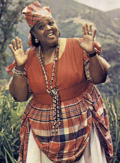 Jamaica's folk ambassador Miss Lou Miss Lou in The National Costume on the cover of her book Jamaica Labrish. A full-flaired skirt made of Madras bandana (predominantly red plaid cotton) material worn usually with a white blouse edged with matching bandana. Headwear varies from bandana wrapped in a special design to straw hat decorated with flowers. Jamaica Culture, Jamaica History, Jamaican People, Jamaican Women, Jamaican Culture, Caribbean Culture, Bob Marley, Kingston, Traditional Outfits