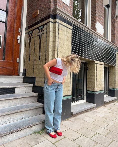 Girl in Amsterdam wearing a white baby tee, low waist straight blue jeans, bright red ballerinas, and a bright red bag, exploring the city streets. White And Red Shoes Outfit, Outfit Ideas Red Shoes, Outfits With Pops Of Red, Jeans And Red Flats Outfit, Red Bags Outfit, Red Bag Outfit Summer, Red Ballet Flats Outfit Summer, Red Flats Outfit Ideas, Red Ballerina Shoes Outfit