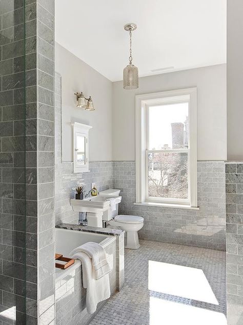 Gray marble subway tiles go halfway up the walls of this beautiful transitional bathroom featuring gray marble basketweave floor tiles illuminated by a mercury glass pendant hung above a bathtub framed by more gray subway tiles while a window on the back wall is partially surrounded by light gray walls. Grey And White Bathroom, Brooklyn Townhouse, Park Slope Brooklyn, Toilet Tiles, Grey Subway Tiles, Marble Subway Tiles, Bathtub Tile, Brooklyn Brownstone, Light Grey Walls