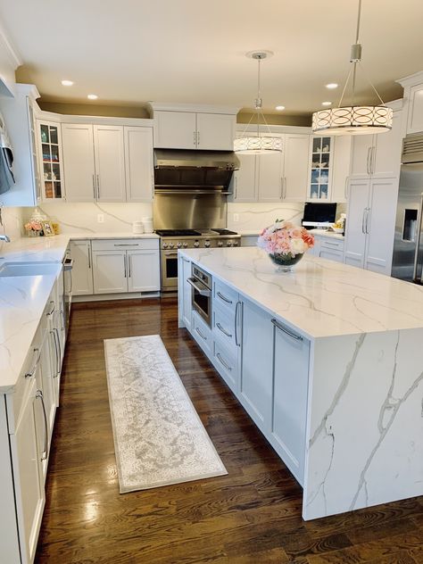 White kitchen done with quartz countertops, backsplash and waterfall island. Stainless appliances and lots of lighting! White Quartz Countertop Waterfall, Waterfall Backsplash Kitchen, Kitchen Design Modern White Quartz Countertops, White Kitchen Cabinets With Waterfall Island, Different Countertops In Kitchen Islands, Kitchens With Waterfall Islands, Modern White Kitchen Design With Island, Kitchen Waterfall Island Ideas, White Kitchen With Waterfall Island