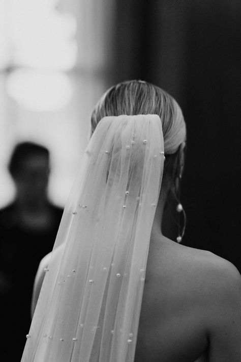 A bride wears a white strapless minimal wedding gown with a sweetheart neckline. Her blonde hair is tied in a low bun over which a long pearl veil is worn. She holds a large bouquet of fluffy white roses. Veil Low Bun, Low Bun Wedding Hair With Veil, Black Tie Aesthetic, Bride Bun, Low Bun Wedding Hair, Blonde Bun, Tower Cake, Large Bouquet, Pearl Veil