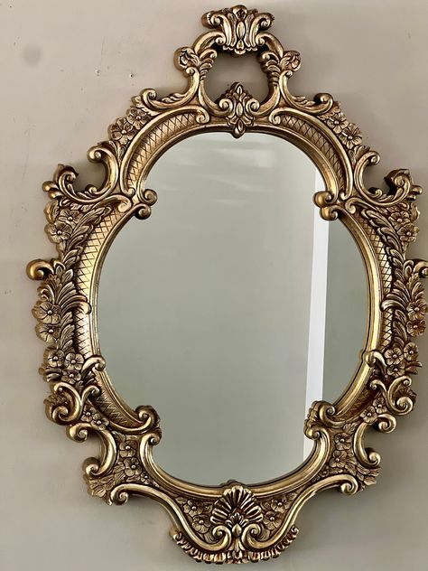 Iconic in its design and reminiscent of Old-Hollywood glamour, this ornately carved, oval, 1960s gold gilt mirror glams up your wall lending an inherent sense of luxury to any space.  Good vintage condition with gilt having acquired a warm patina. No cracks of any kind. Gorgeous Gold Gilt Heavy Plastic Composite Frame. Some visible shading and wear of gold gilt paint on frame and outer sides, which only adds glamour to the warm patina. One clamp for hanging the mirror is broken but the mirror ca Gold Princess Mirror, Ornate Wall Mirror, French Gold Mirror, Big Gold Mirrors, Oval Vintage Mirror, Gold Apartment Aesthetic, Gilded Vintage Decor, Vintage Gold Decor, Gold Aesthetic Home Decor