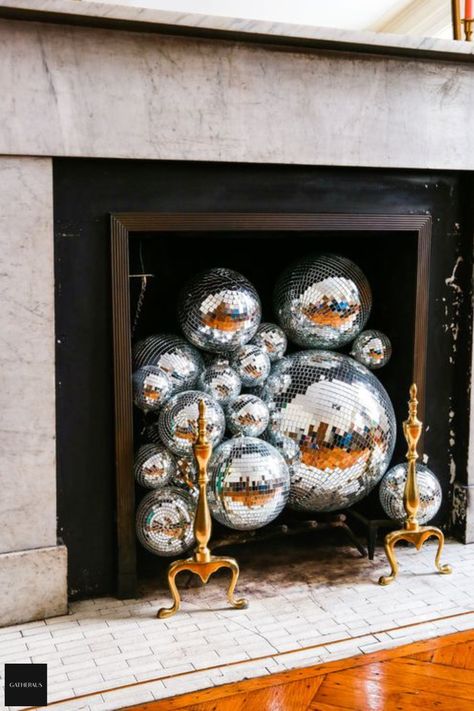 Looking for a festive way to decorate an empty fireplace for your New Year's Eve party? Check out this easy decorating idea - just fill your fireplace with disco balls! This will add some fun and sparkle to your celebration. Happy New Year! For more ideas on decorating your unused fireplace, check out our latest post. Disco Balls Fireplace, Disco Balls In Fireplace, Disco Ball Fireplace, Fireplace Disco Ball, Ceramic Fire Balls Fireplace, Melted Disco Ball Decor, Ball Fireplace, Copper Disco Ball, Empty Fireplace