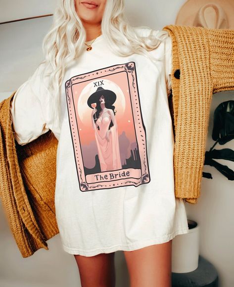 A woman wearing an oversized t shirt with an image of a tarot card called the bride in orange and pink tones. Very boho in style Grunge Bachelorette Party Outfit, Goth Bachelorette Party, Salem Bachelorette, Bohemian Bachelorette Party, Goth Bachelorette, Witchy Bachelorette Party, Witch Bride, Witchy Bride, Nola Bachelorette Party