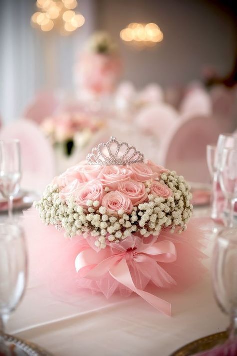 A baby shower centerpiece on a white tablecloth showcasing a tiara atop a bouquet of pink roses and white baby's breath, surrounded by soft pink tulle and tied with a pink ribbon, makes for charming centerpiece ideas at a baby shower or other formal event. Baby Shower Centerpiece Ideas, Small Tiara, Tiny Castle, Princess Centerpieces, Baby Shower Princess Theme, Storybook Theme, Pastel Balloons, Elegant Baby Shower, Unique Centerpieces