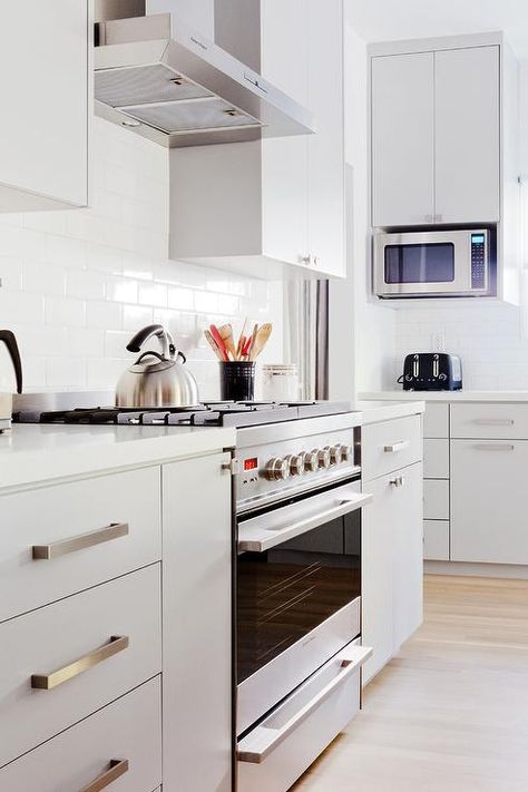 Light gray flat panel drawers painted in Farrow & Ball Pavilion Gray are fitted with satin nickel pulls and a white quartz countertop and flank a stainless steel oven rage fixed against an all white subway tile backsplash beneath a stainless steel hood. Flat Front Kitchen Cabinets, Flat Panel Kitchen Cabinets, Flat Cabinets, Pavilion Grey, Espresso Kitchen Cabinets, Rustic Backsplash, Espresso Kitchen, Farmhouse Backsplash, Beadboard Backsplash