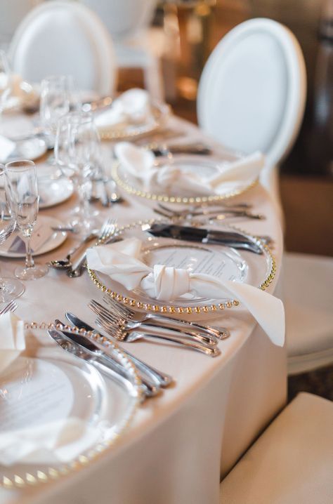 Elegant white and gold wedding place setting with gold ball edge glass charger plate, knotted satin napkin, and silverware at the Liberty Grand. Photo by Sandra Monaco.  #WhiteandGoldPlaceSetting #WeddingPlaceSettingInspiration #WeddingPlaceSettingIdeas #BallEdgeGlassChargerPlate #WeddingGuestTableInspiration #WeddingGuestTableIdeas #TorontoWedding Gold Chargers And Silver Silverware, Charger Plate With Napkin, Gold Charger With Silver Flatware, Gold Rim Charger Plate Wedding Tables, Wedding Flatware Setting, Glass Charger Plates Wedding, Satin Napkins Wedding, Charger And Napkin Place Setting, Gold Napkins Wedding Table Settings