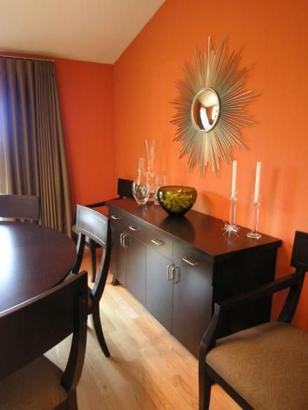 The dark wood dining set and buffet are a sweet complement to pumpkin orange walls in this chic dining room. A gold sunburst mirror echoes the natural tones of the orange walls, while enhancing the overall color scheme. Clear, glass accessories are a neutral accompaniment to the room and avoid interrupting the vibrant wall color. Design by Velvet Hammerschmidt Orange Dining Room, Living Room Decor On A Budget, Orange Rooms, Chic Dining Room, Living Room Orange, Room Blue, Orange Decor, Mirror On The Wall, Trendy Living Rooms