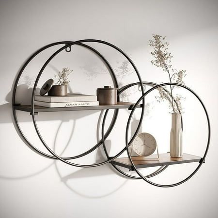 Presenting the Isabella Black Round Wood-Metal Modern Wall Shelfa masterful marriage of form and function. This uniquely designed wall shelf showcases two rectangular wooden bases, housed within an intriguing framework of black interlocking metal circles. The staggered arrangement not only offers a multi-level display shelf for your keepsakes but also infuses your space with a modern, geometric flair. Whether you're looking to embellish your living room, bathroom, or office, the Isabella Wood-Metal Shelf delivers both visual appeal and practical storage solutions, embodying the best of contemporary design. Size: 17.25" H x 23" W x 5.5" D.  Color: Brown. Steel Pipe Shelving, Room Decor Bedroom Rose Gold, Long Wall Shelves, Circle Shelf, Gold Room Decor, Wall Storage Shelves, White Floating Shelves, Modern Wall Shelf, Designed Wall