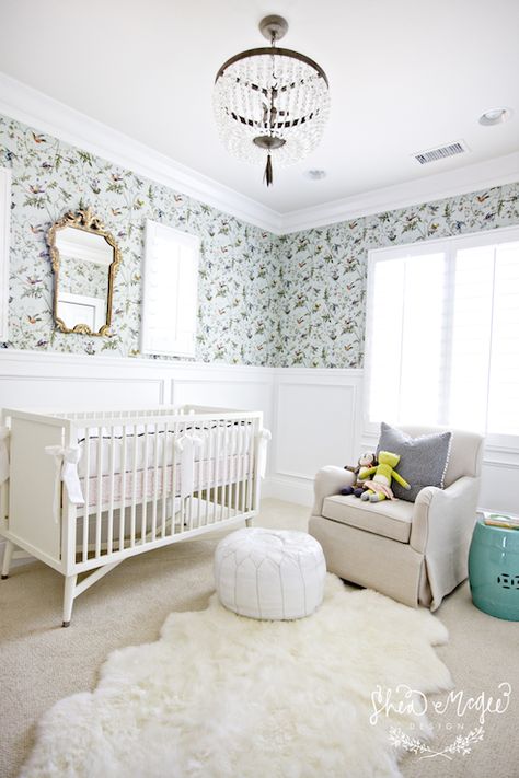 Lovely nursery features aviary wallpaper on top half of wall and wainscoting on bottom half of wall framing gilt ornate mirror over white traditional crib dressed in white and pink crib bedding. Girl's nursery with white beaded glass chandelier over oatmeal linen glider accented with gray pillow and paired with turquoise stool and white Moroccan leather pouf over sheepskin rug layered over beige wall to wall carpeting. Mcgee Design, Transitional Nursery, Nursery Window, Shea Mcgee, Baby Nurseries, Bird Nursery, Babies Room, House Of Turquoise, Nursery Room Design