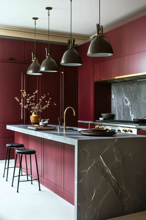 A burgundy kitchen with white floors, a burgundy Island and charcoal gray counter tops and light fixtures. Burgandy Interior Design, Burgundy Marble Kitchen, Red Island Kitchen, Bold Marble Kitchen, Dark Red Kitchen Cabinets, Burgundy Mood Board, Kitchen Burgundy, Burgundy Interior Design, Burgundy Kitchen Cabinets