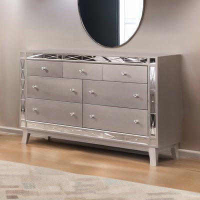 With this elegant dresser, your bedroom will exude glam and sophistication. Constructed from poplar wood, Asian hardwood, and select woods in a chic, mercury-silver metallic finish, the dresser features seven drawers that provide more than enough space for all of your clothing and accessories. Its mirrored panel accent borders the front of a dresser to pair beautifully with the finish and provide more light and a greater sense of depth to your room. With the addition of this dresser, you will cr Glass Dresser Bedroom, Grey Dresser Bedroom, Silver Bedroom Furniture, White And Silver Bedroom, Silver Living Room, Mirror Dresser, Silver Dresser, Silver Bedroom, Mirrored Bedroom Furniture