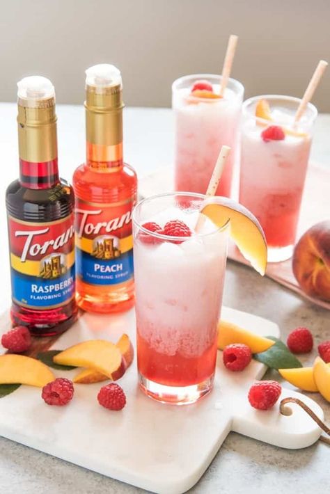 These Italian cream sodas are refreshing, creamy, and made for summertime! Create an Italian soda bar for your next party, or just make one for yourself to enjoy on a hot day. | raspberry peach italian cream soda recipe | raspberry italian cream soda | peach italian cream soda | how to make italian cream soda | how to make an italian cream soda | italian cream soda recipe how to make | homemade italian cream soda recipe | recipe for italian cream soda Torani Syrup Recipes, Torani Recipes, Italian Soda Bar, Italian Cream Soda, Torani Syrup, Lemonade Punch, Soda Bar, Italian Cream, Peach Syrup