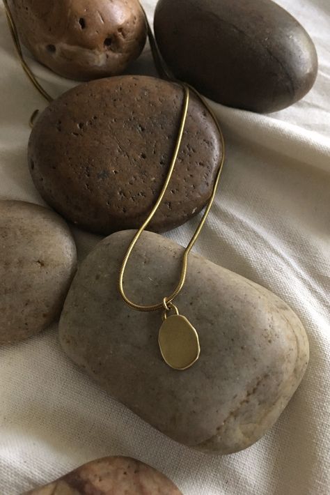 This classic brass necklace features an organic shaped pendant suspended on a snake chain. Named after 'pebble' in Arabic, it is an ode to both the structured and natural world. The more delicate sister style to the Hasaa Major Necklace. Details: 18” chain Solid brass Handcrafted artisan quality Lightweight, comfortable Learn about brass jewelry care tips here. Process: This piece is fabricated by hand in St. Louis, MO using domestically-sourced, durable solid brass. Because this piece is made t Artistic Jewelry Photography, Jewelry Pictures Photography, Pendant Photography Ideas, Jewelry Props Photography, Jewelry Still Life Photography, Jewelry Photography Styling Instagram, Jewellery Product Shoot, Jewelery Shoot, Necklace Shoot