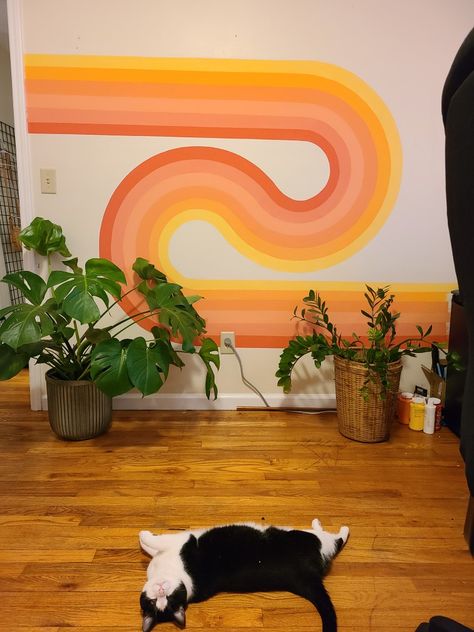 70s wavy wall art with pink peach yellow orange tones in a rainbow looping together with a big monstera plant and zz plant on the right wooden floor with a very cute black and white Cat laying on the floor looking at the camera Aesthetic Walls Painted, Aesthetic Room Wall Painting, 70s Wall Mural Retro, Wall Mural Design Ideas, Supergraphics 70s, 70s Wavy Wall Art, Painting Ideas On Wall Aesthetic, Bedroom 70s Aesthetic, Groovy Wall Painting