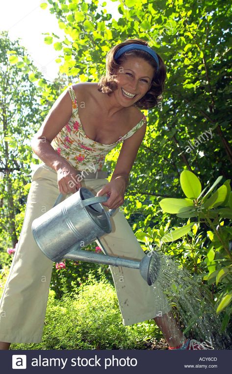 smiling woman in garden watering some plants with a watering can Stock Photo Holding Watering Can Reference, Person Watering Plants Reference, Watering Plants Reference, Person Watering Plants, Woman Watering Plants, Fantasy Cafe, Woman In Garden, Irl References, Watering Lawn