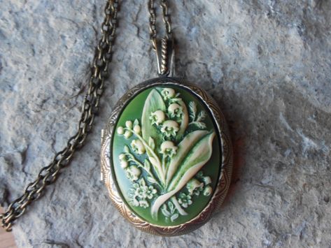 Beautiful cameo locket.  The cameo is a gorgeous lily of the valley. Stunning colors, each cameo is individually hand painted and antiqued, each an original.  The bronze, silver plated and gold plated lockets are Victorian style with beautiful etching on both the front and back about 2" long.  They can hold two photos or a treasured keepsake.  Pass down from generation to generation.  The bronze locket includes a 24" link chain with a lobster claw clasp, and the silver and gold includes a 24" si Etiquette Vintage, Funky Jewelry, April 26, Coin Jewelry, Jewelry Inspo, Dream Jewelry, Locket Necklace, Pretty Jewellery, Lily Of The Valley