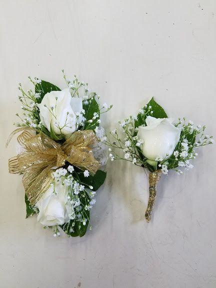 White roses, baby's breath, green leaves and gold trim wrist corsage and boutonniere. White And Green Corsage And Boutonniere, Homecoming Corsage For Green Dress, White Rose Corsage And Boutonniere, White Green Corsage, White Flower Corsage And Boutonniere, Sage Green Corsage And Boutonniere, White Corsage And Boutonniere Set, Corsage Prom White And Gold, Green And Gold Corsage Prom