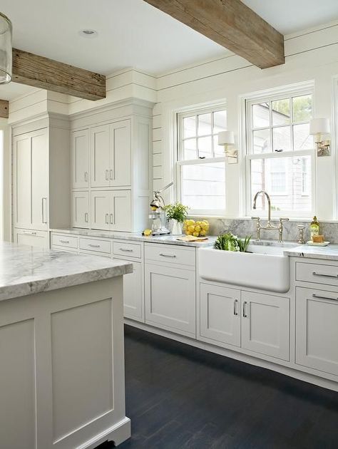 Light gray and white kitchen with a classic design features stacked light gray shaker cabinets accented with nickel pulls and fitted with Super White Quartzite countertops holding a farmhouse sink and polished nickel, deck bridge mount, gooseneck faucet under single hung windows separated by small sconces mounted to ivory shiplap walls supporting rustic wood ceiling beams hung over dark stained oak wood floors. Light Grey Kitchens, Ship Lap, Rustic Kitchen Cabinets, Gray And White Kitchen, Farmhouse Kitchen Cabinets, Casa Vintage, Rustic Farmhouse Kitchen, Farmhouse Ideas, White Kitchen Design