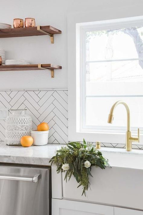 A farmhouse sink with a brushed gold gooseneck faucet is positioned beneath a window partially framed by white herringbone tiles. White Glass Backsplash, Chevron Backsplash, White Herringbone Tile, White Kitchen Backsplash, Tile Design Pattern, Kitchen Tiles Design, Glass Tile Backsplash, White Backsplash, Glass Backsplash