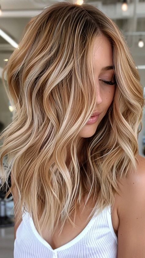 Woman with wavy blonde hair highlights, wearing a white top, in a modern salon. Brown Hair After Red, Cherry And Blonde Highlights, Strawberry Hair Color Blonde, Blonde And Auburn Highlights On Brown Hair, Dark Blonde Hair With Red Undertones, Low Maintenance Winter Blonde, Copper Babylights On Blonde Hair, Brunette With Blonde And Red, Blonde Hair Color Ideas With Lowlights