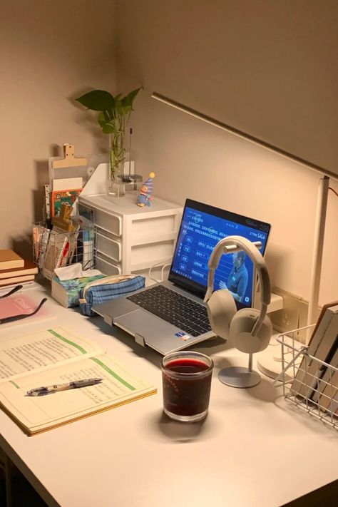 A minimalist study desk setup with a laptop, open notebook, reading lamp, headphones, and a calming candle. The desk also includes books, a plant, and organizational drawers, creating a warm and inviting space perfect for studying or working Simple Study Table Ideas Student, Simple Office Setup, Simple Desk Organization, Study Set Up, Student Desk Setup, Minimalist Study Table, Setup Notebook, Simple Desk Setup, Study Desk Setup