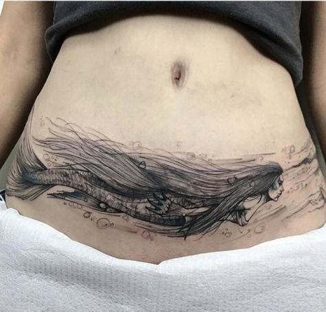 For the person who loves mermaids comes this stunning mermaid tattoo for tummy tuck scars! The mermaid is created in black ink and extends throughout the width of the stomach and onto the hip area. The mermaid’s long, flowing hair expertly hides all elements of the scar, while the bubbles and flowing water add to the final look. Lower Abdomen Tattoo, C Section Scar Tattoo, Lower Belly Tattoos, Side Stomach Tattoos, Abdomen Tattoo, Lower Stomach Tattoos, Tummy Tattoo, Tattoo Over Scar, Stomach Tattoos Women