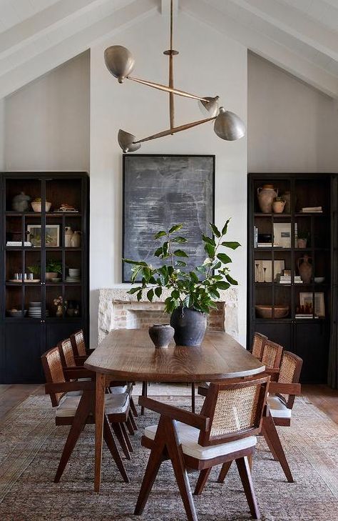 An oval oak dining table sits on a black and brown vintage rug surround by rope and wood dining chairs and is positioned in front of a rustic stone fireplace fixed beneath an abstract black art piece. Dark Wood Dining Room, Oval Dining Room Table, Dark Wood Dining Table, Dark Dining Room, Dark Wood Table, Cottage Dining Rooms, Brown Dining Table, Wood Dining Room Table, Wood Dining Room