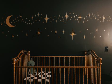 Black and gold space themed nursery. Stars and alien plushie with checkboard blanket. Planet Themed Nursery, Galaxy Nursery Ideas, Moody Maximalist Nursery, Alien Nursery Theme, Dark Fairytale Nursery, Astrology Nursery Theme, Night Themed Nursery, Star Nursery Girl, Witchy Baby Nursery