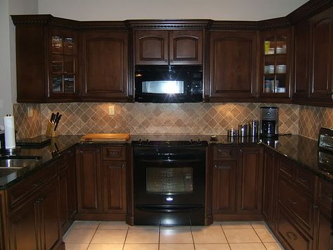 Brown kitchen cabinets with dark countertop and lighter colored tile backsplash and floors. I would have done a Yorba lead gray floor and green or blue glass backsplash. Popular Kitchen Colors, Backsplash With Dark Cabinets, Espresso Kitchen Cabinets, Black Appliances Kitchen, Espresso Kitchen, Brown Kitchen Cabinets, Kabinet Dapur, Black Appliances, Brown Cabinets